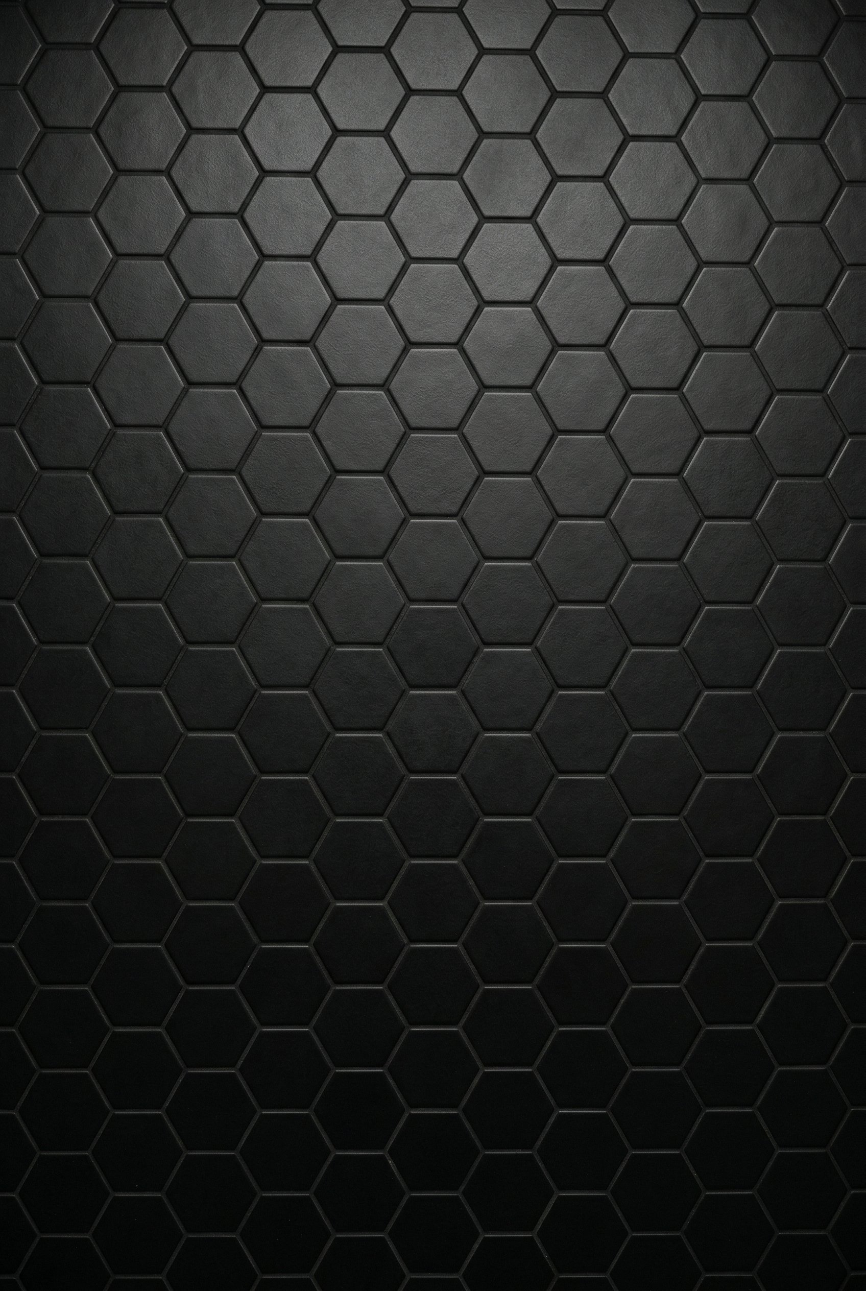 Photorealistic interior photo. Close up of matte black hexagonal floor tiles with matching black grout. Seamless monochromatic look. Editorial photography style, top-down angle, no people visible.