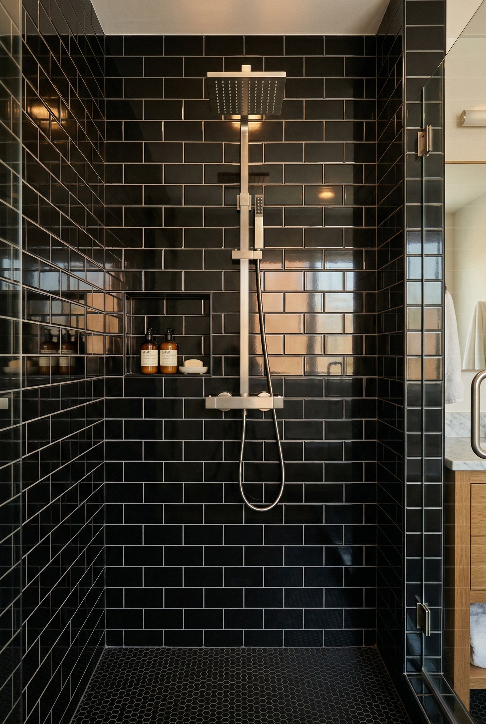 Photorealistic interior photo. High-gloss black subway tiles in a shower enclosure, reflecting warm ambient light. Clean grout lines. Editorial photography style, straight-on angle, no people visible.
