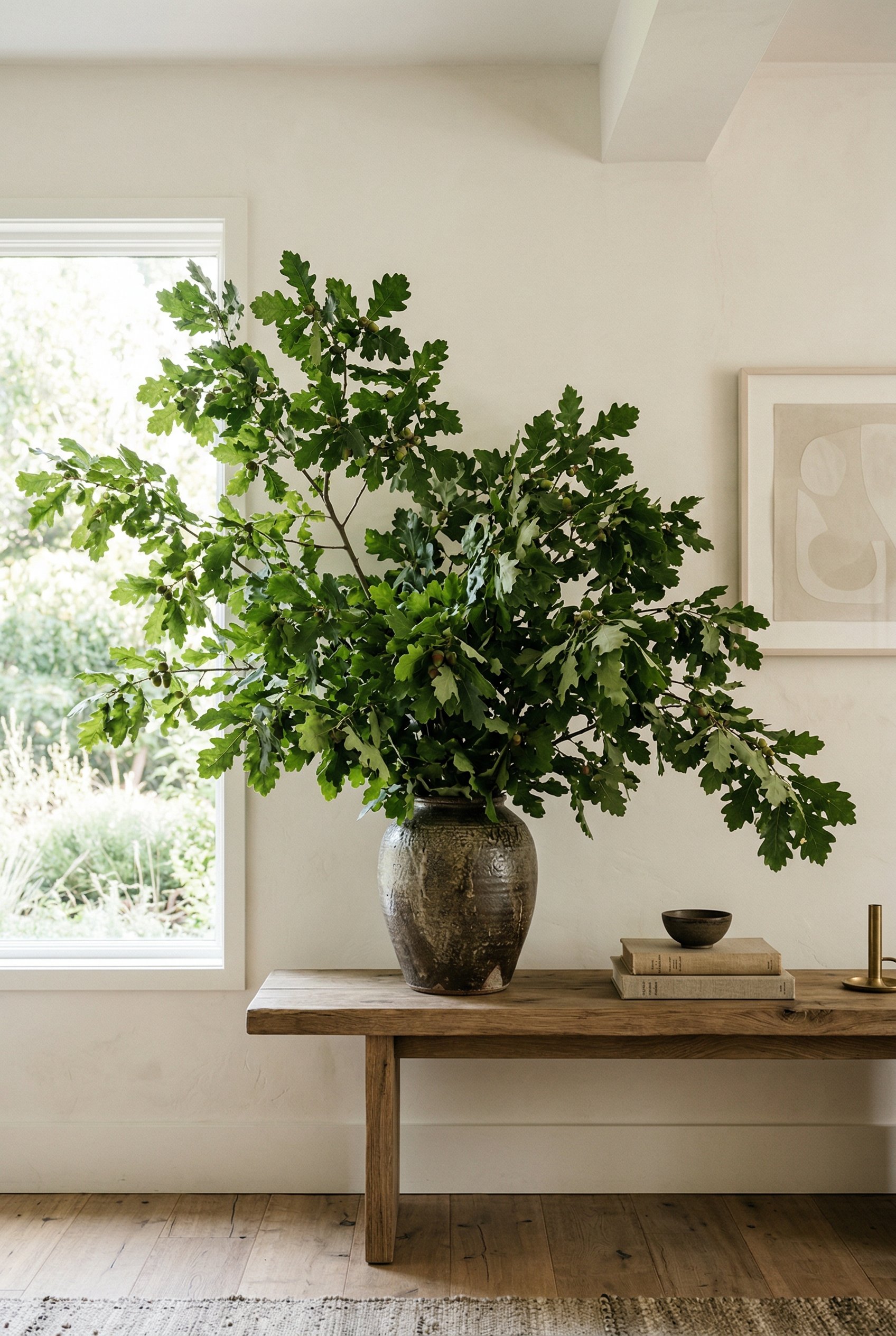 Photorealistic interior photo. Massive foraged leafy oak branches in a rustic heavy stoneware vase sitting on a console table, minimalist background, bright natural lighting. Editorial photography sty
