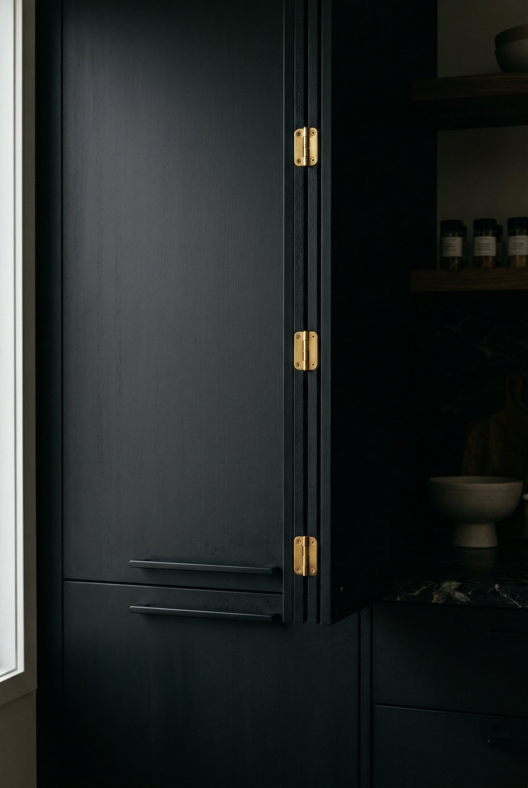 Photorealistic interior photo. Moody black kitchen cabinets with matching matte black pulls, subtle gold cabinet hinges peeking out. Cinematic lighting highlighting the gold hinges, straight-on close-