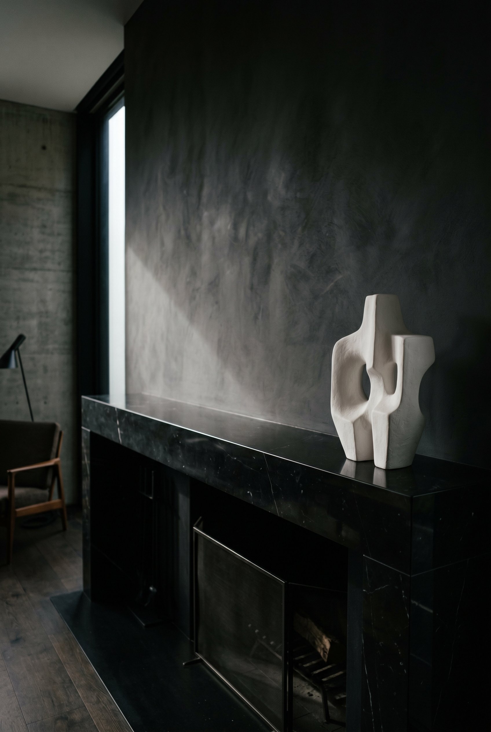 Photorealistic interior photo. Ultra-sleek black marble mantel with extreme negative space. A single abstract white plaster sculpture sits on the far right. The rest of the mantel is completely bare. 