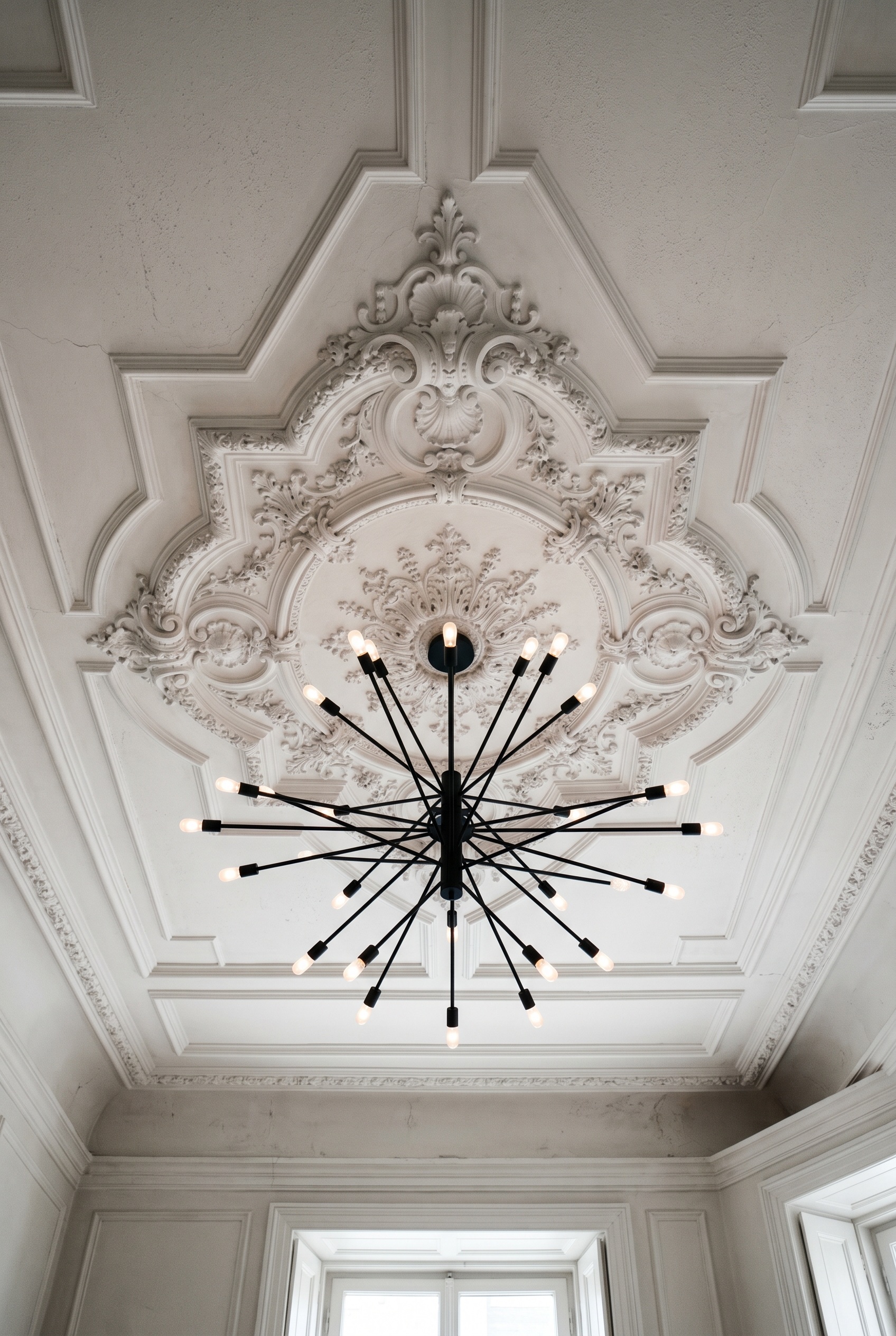 Photorealistic interior photo. Looking up at an ornate white plaster ceiling medallion holding a stark, modern matte black multi-arm sputnik chandelier. High contrast architectural tension. Soft ambie